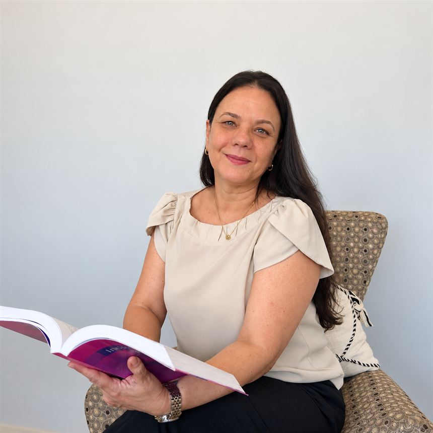 Monica Ribeiro Oliveira sentada em poltrona com um livro aberto